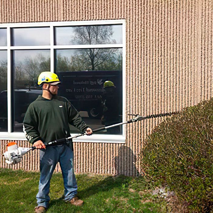A man is standing in front of a building holding a hedge trimmer.