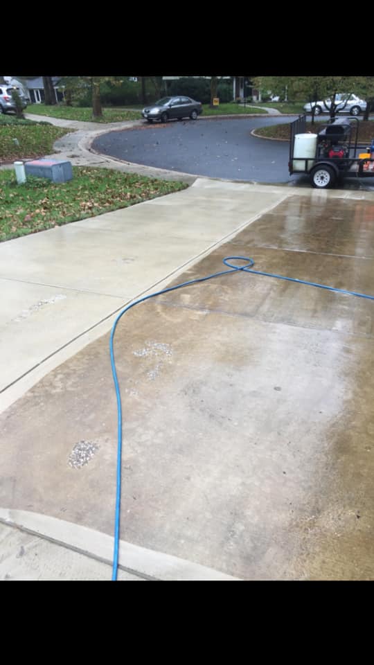 A concrete driveway is being cleaned with a pressure washer.