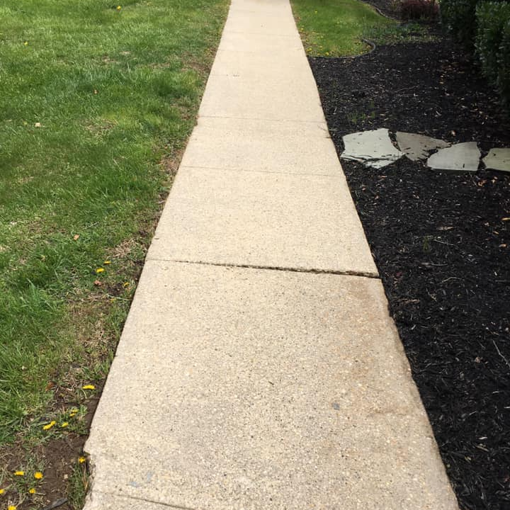 A sidewalk with a grassy area on the side and a black mulch on the other side.