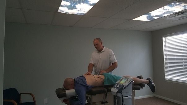 Therapist working on a patient lying face down on a treatment table in a clinic room.