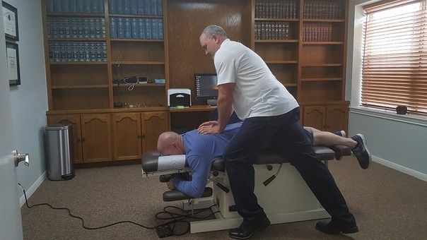 Man adjusting a person on a chiropractic table in an office with bookshelves