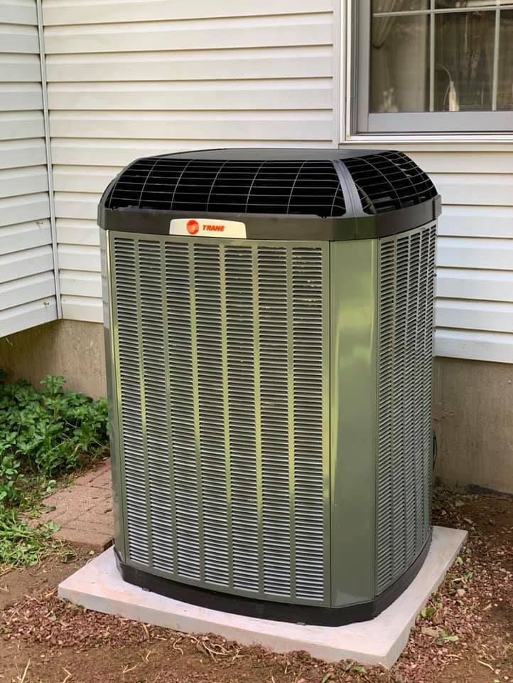 Air conditioner unit on concrete pad next to a house with beige siding and a window.