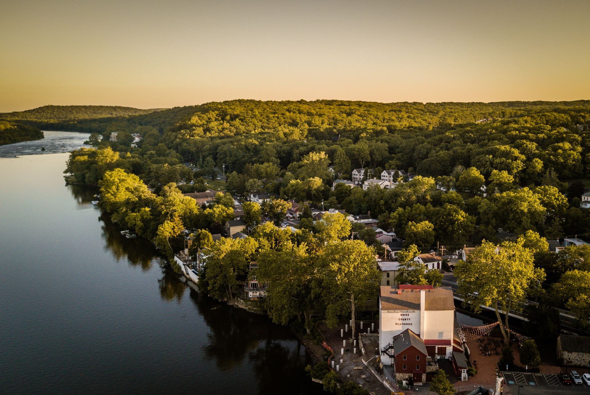 Aerial view of a riverfront town with lush green trees and buildings, at sunset.