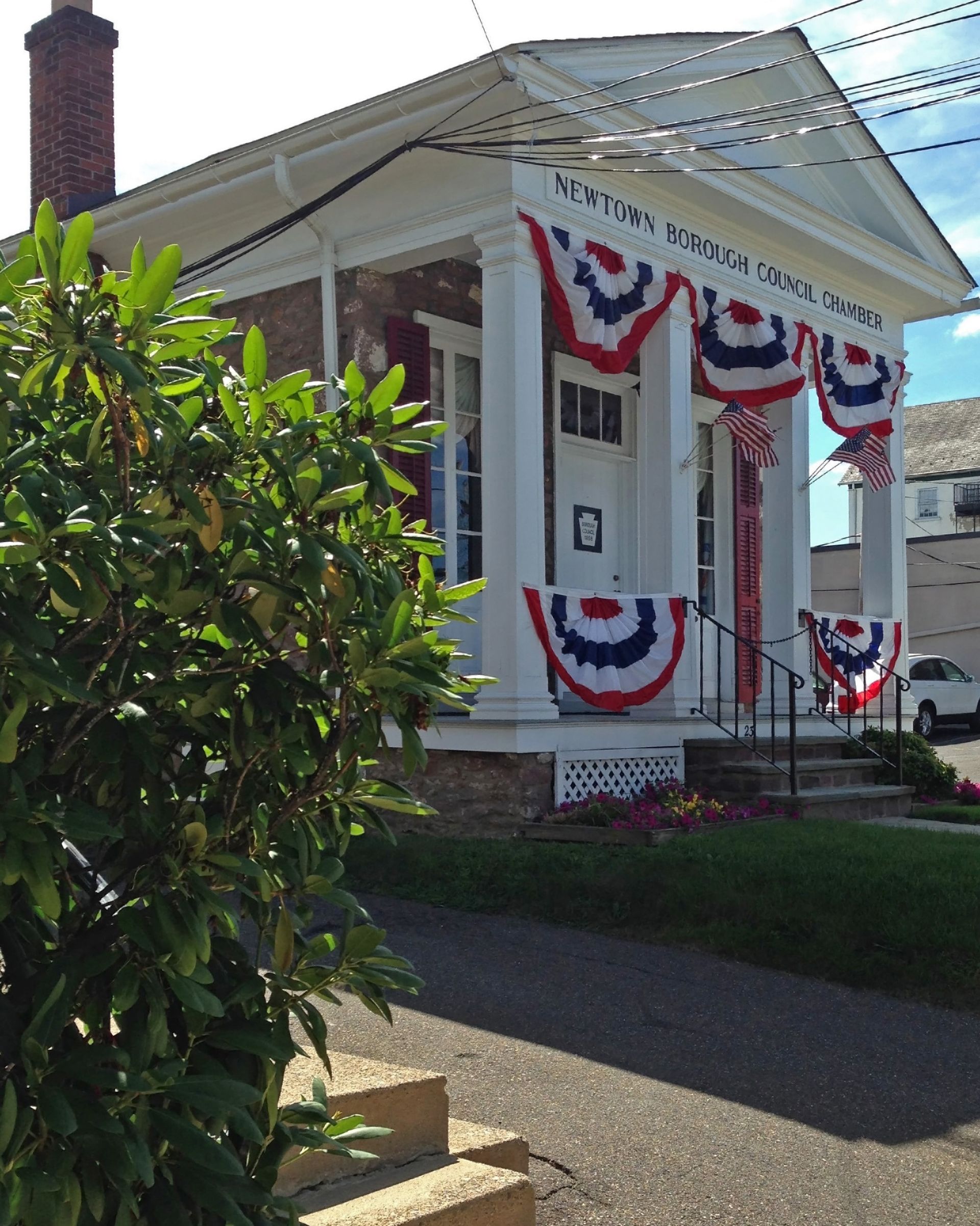 Small white building decorated with red, white, and blue bunting; a stone exterior and porch with pillars.