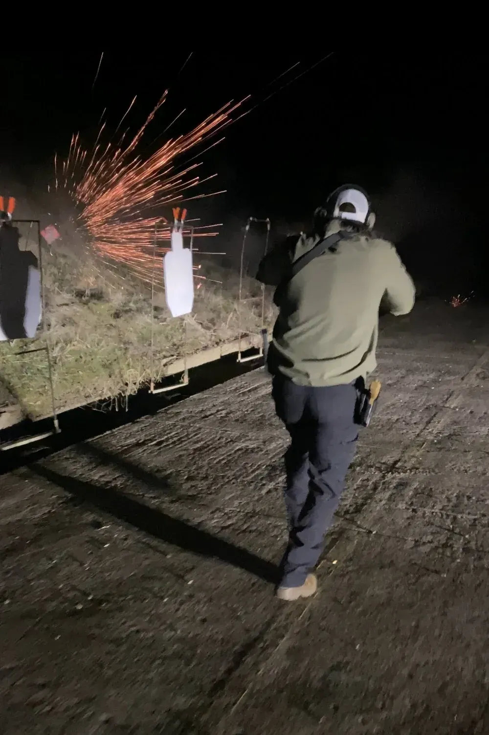 Man firing rifle at night, sparks flying.