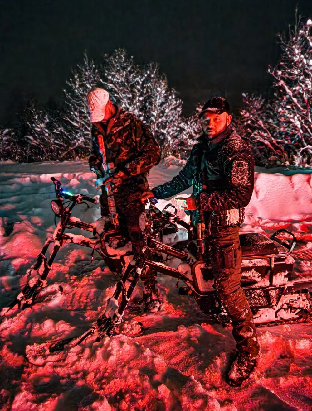 Two people with fat tire bikes in snow at night, lit by red light.