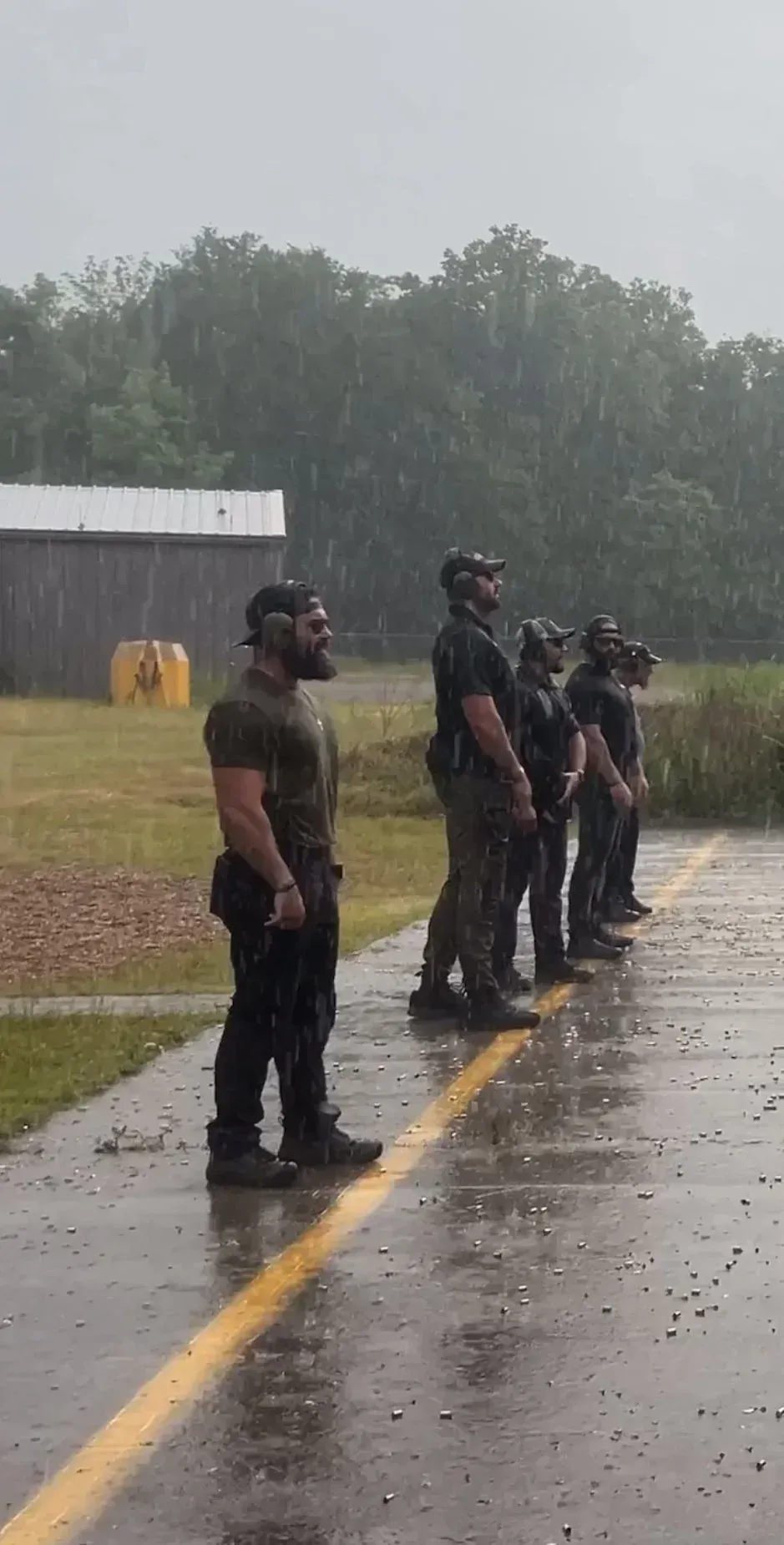 Men in tactical gear stand in the rain on a range.