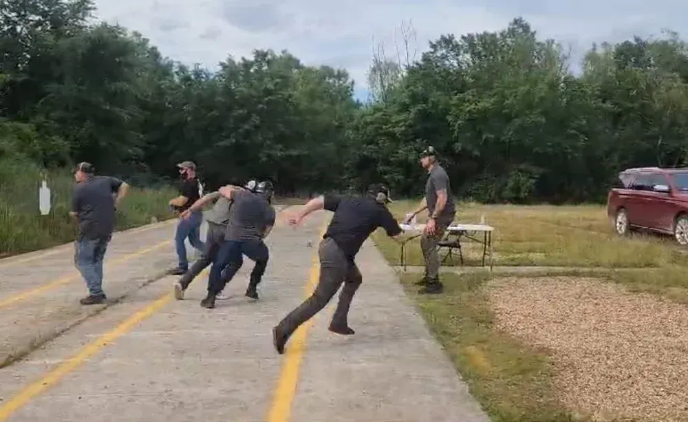 People running, some in dark clothing, on a paved area with a table and trees in the background.