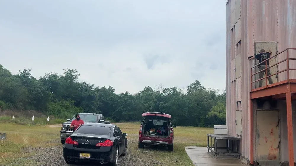 Vehicles parked outside a training building as a person holds a weapon in the doorway.