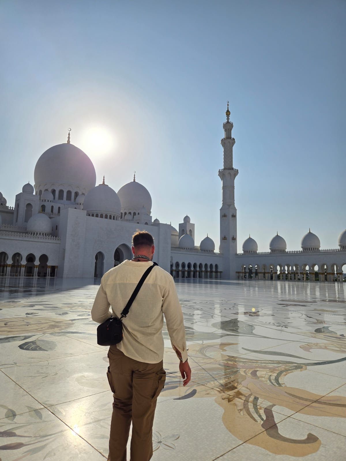 Man walking towards Sheikh Zayed Mosque in Abu Dhabi, white domes, minaret, and sunny sky.