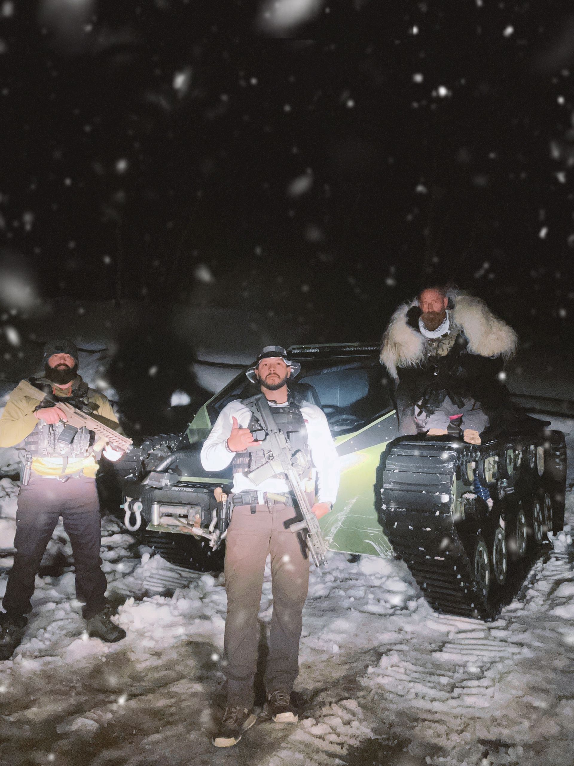 Three men with guns pose by a tracked vehicle in a snowy, nighttime scene.