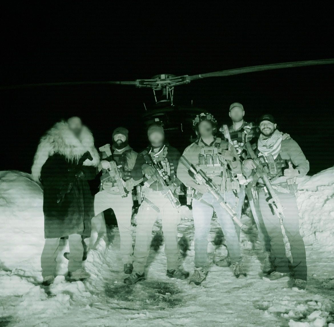 Group of armed soldiers stand in snowy area near a helicopter at night, lit with green night vision.