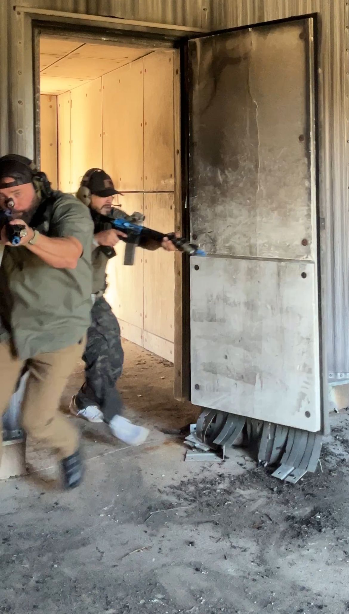 Two armed men in tactical gear breach a door, one aiming a rifle.