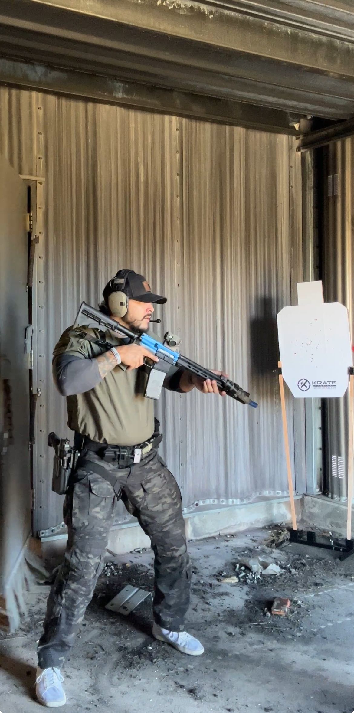 Man in tactical gear aiming rifle at target in a shooting range.