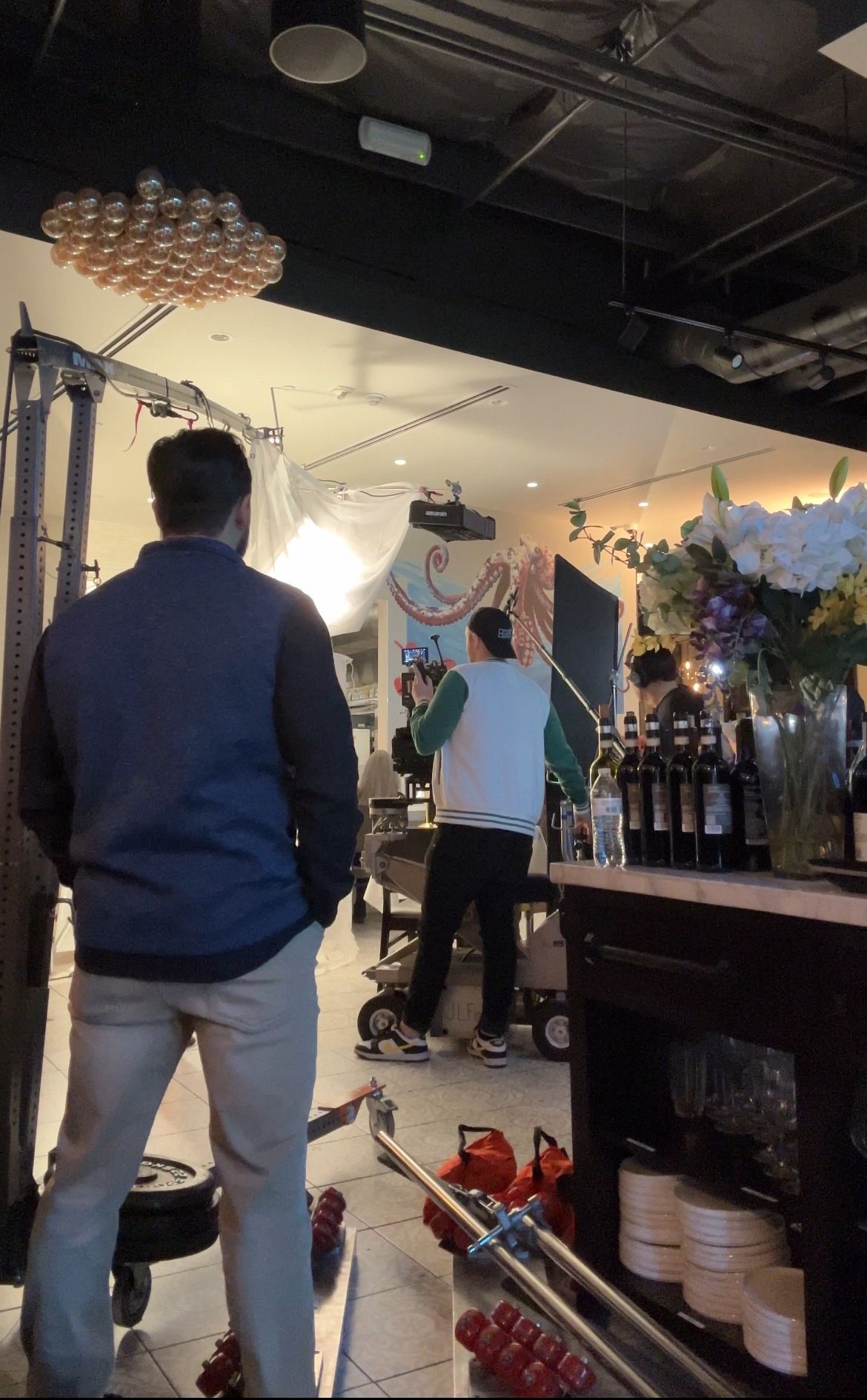 Two men in a store, one looking at a machine, the other facing a backdrop, surrounded by bottles and lights.