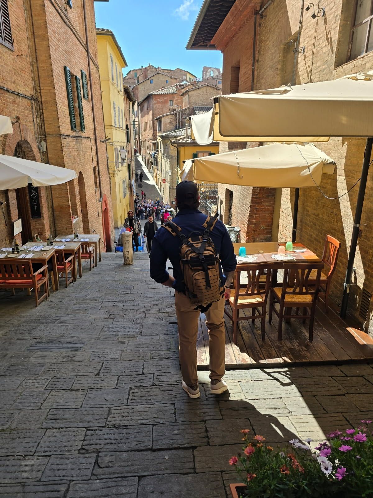 Man walking down a cobblestone street in Siena, Italy, lined with restaurants.