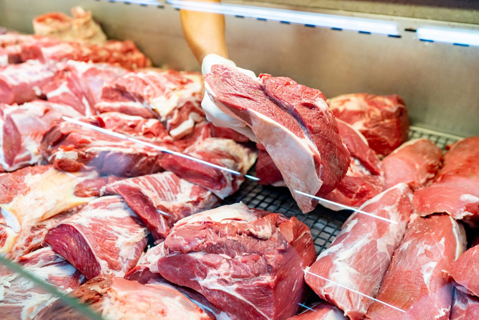 A display case filled with lots of raw meat in a butcher shop.