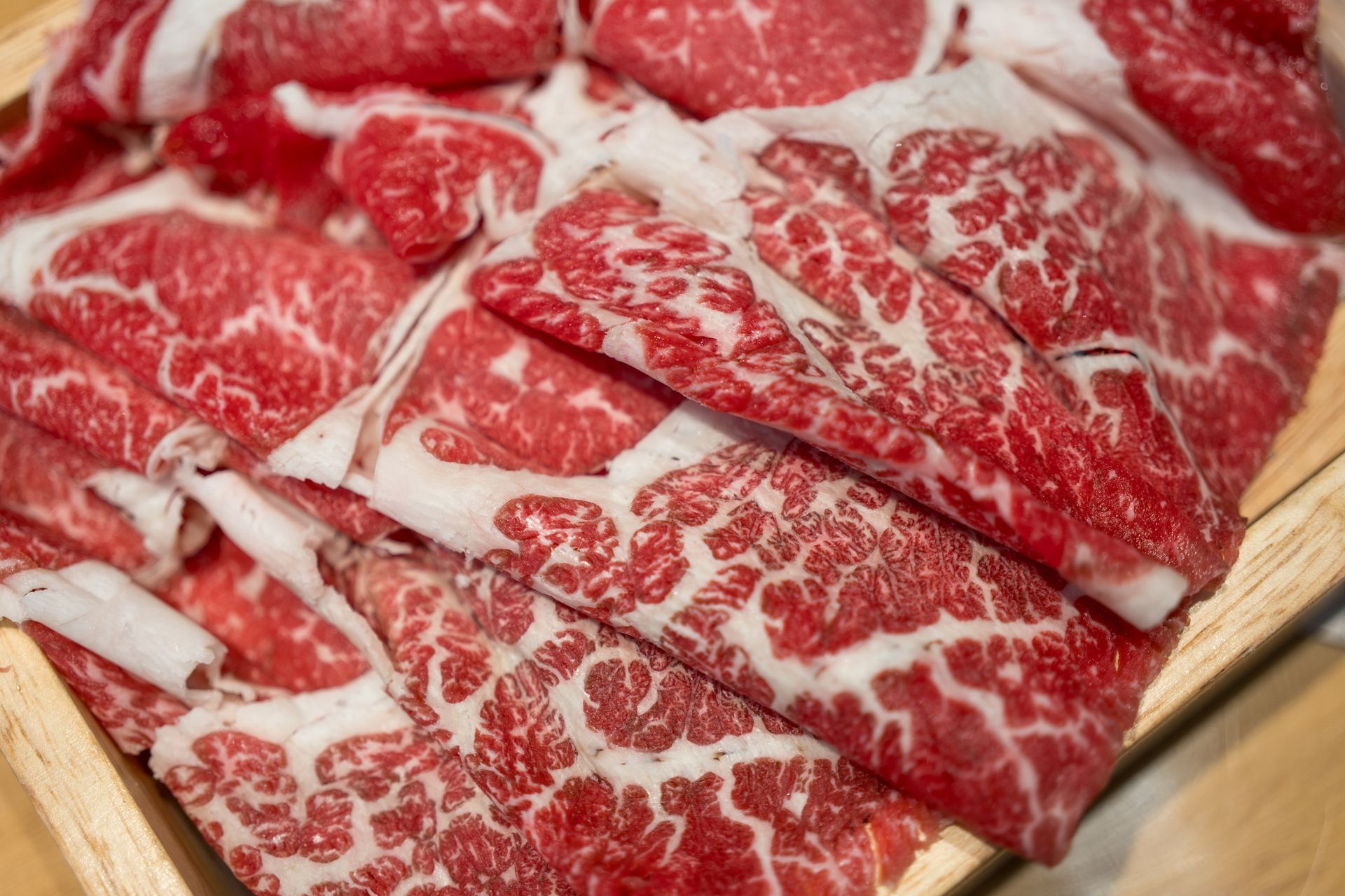 A close up of sliced beef on a wooden tray.