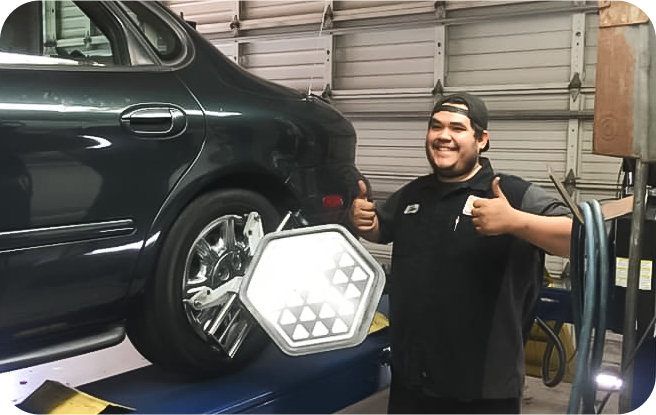 A man is giving a thumbs up in front of a car in a garage. | Friendly Auto Centers