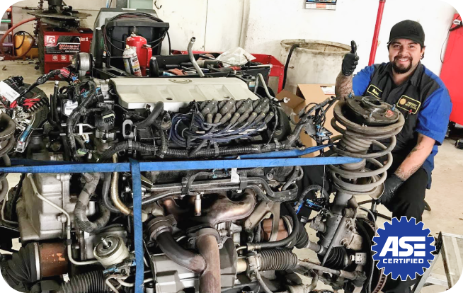 A man is sitting in front of a large engine in a garage. | Friendly Auto Centers