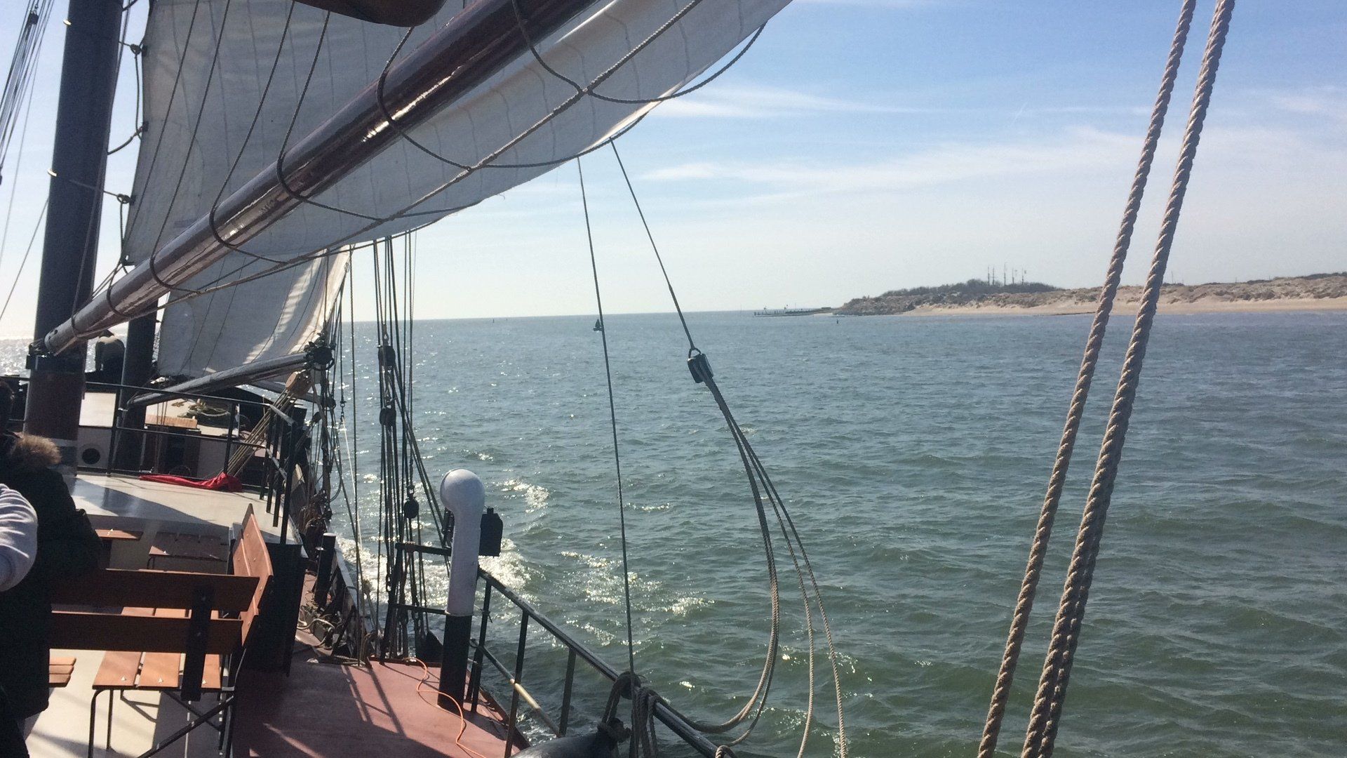 Segelboot segelt auf dem Wasser, Küstenlinie in der Ferne. Blick vom Deck mit Seilen und Segeln.