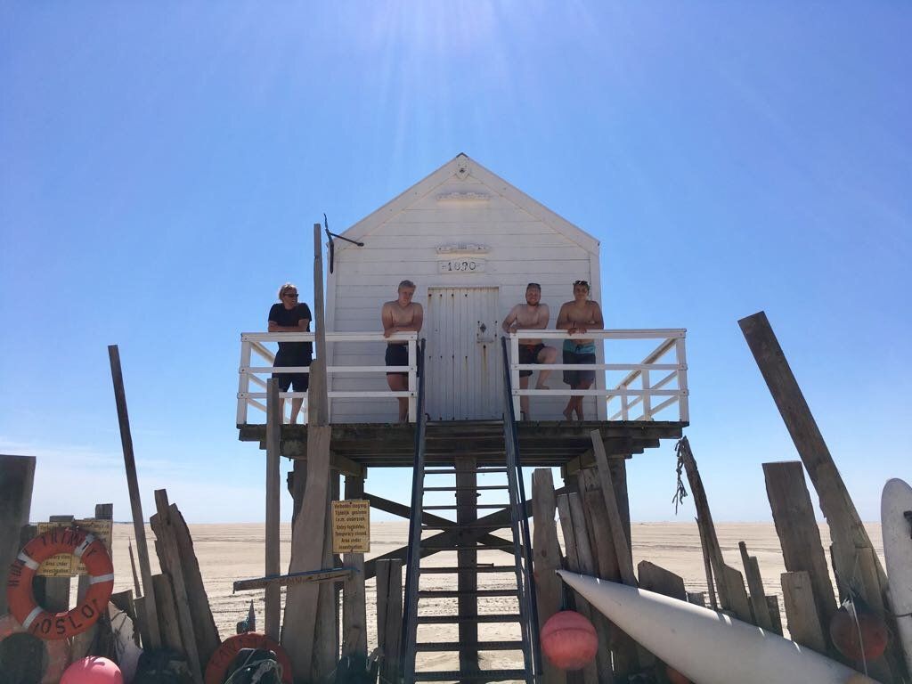 Menschen auf einer erhöhten weißen Rettungsschwimmerhütte am Strand von Vlieland vor einem klaren blauen Himmel.