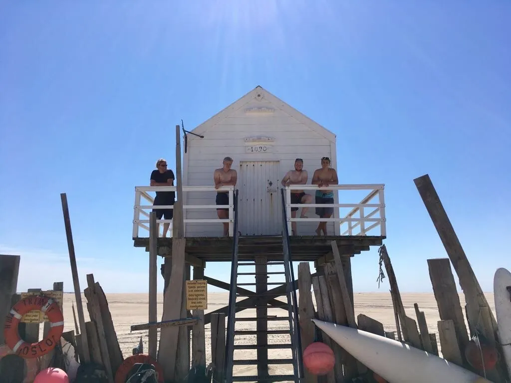 Menschen auf einer erhöhten weißen Rettungsschwimmerhütte am Strand von Vlieland vor einem klaren blauen Himmel.