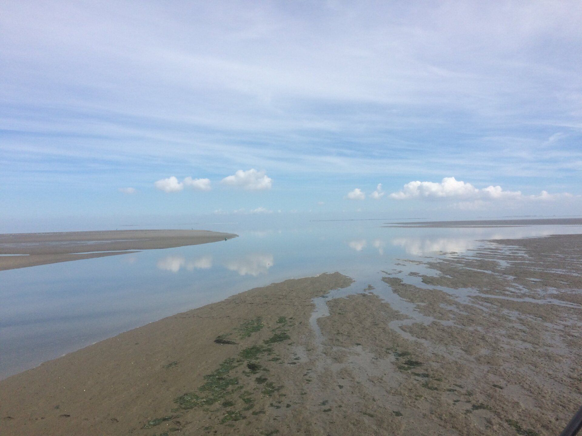 Unter einem teilweise bewölkten Himmel trifft eine sandige Küste auf ruhiges Wasser.