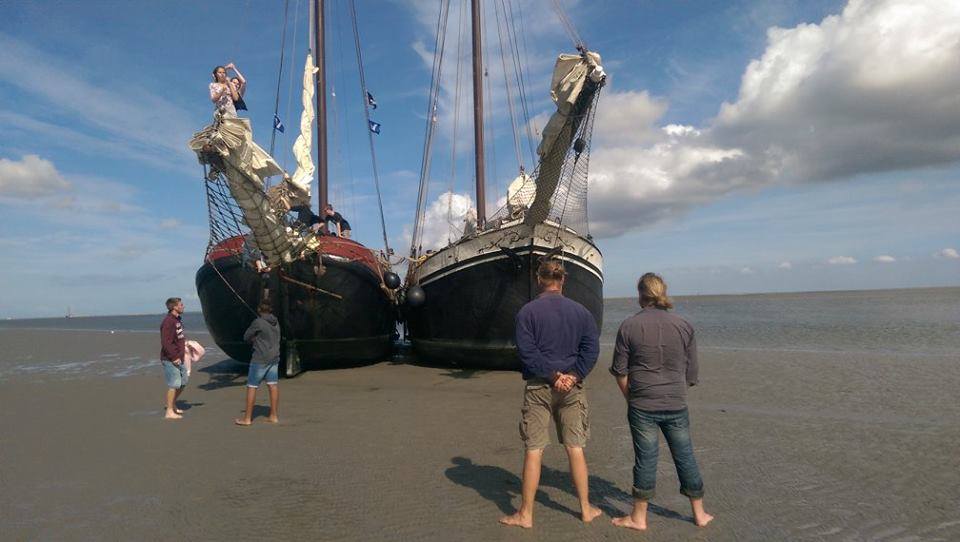 Zwei Segelboote auf Sand, Menschen stehen in der Nähe, bewölkter Himmel.