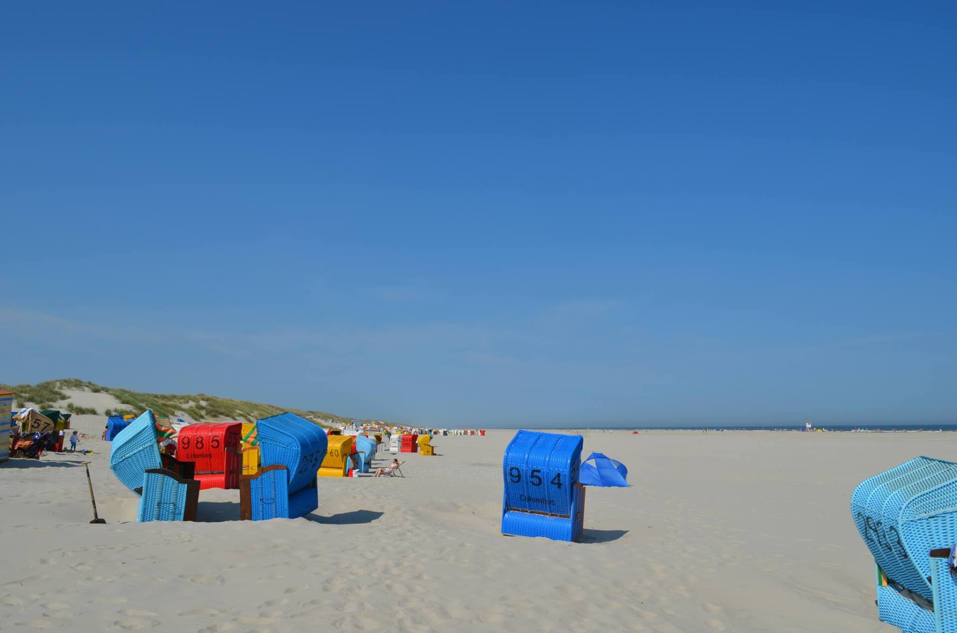 Strand mit bunten Sonnenschirmen unter einem klaren blauen Himmel.