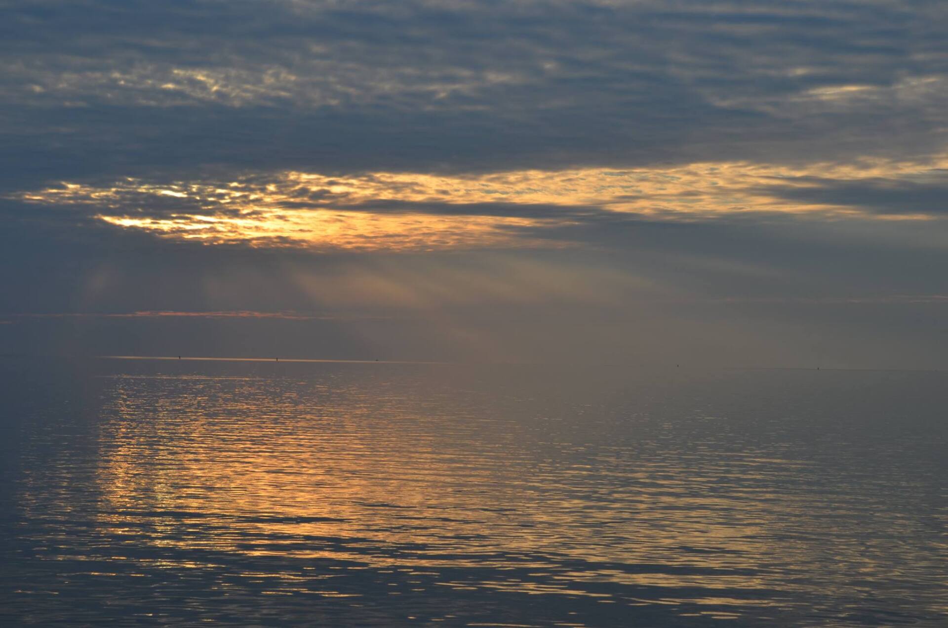 Die Sonne lugt durch die Wolken über einem schimmernden Ozean. Goldenes Licht spiegelt sich auf dem Wasser.