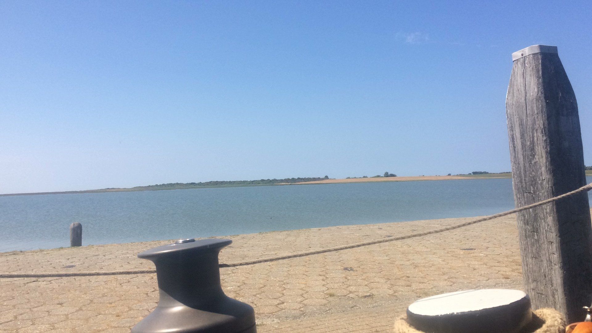 Sandstrandszene mit ruhigem Wasser, blauem Himmel und Holzpfosten mit Seil.