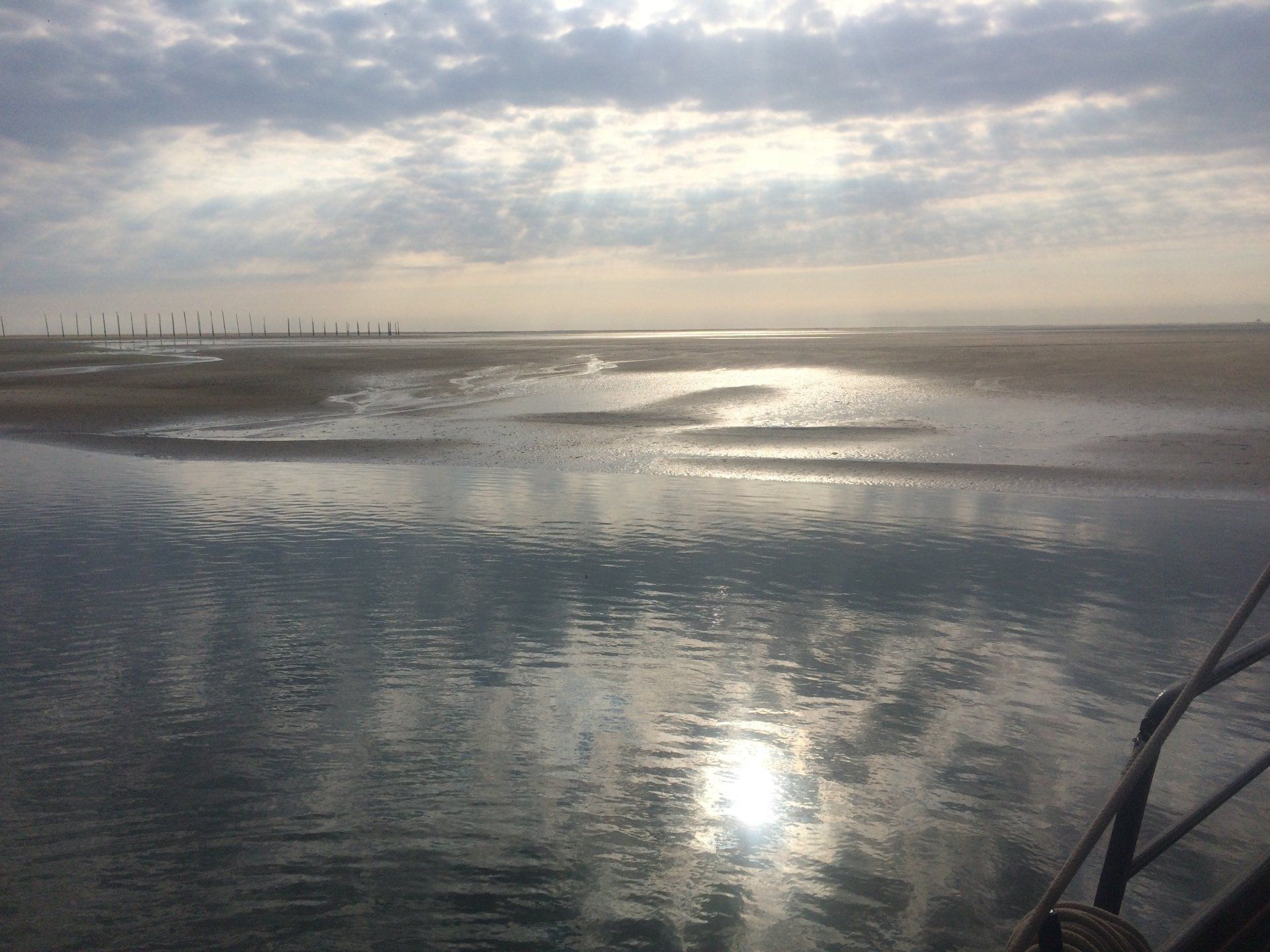Ruhiges Wasser spiegelt einen bewölkten Himmel und einen sandigen Strand wider.