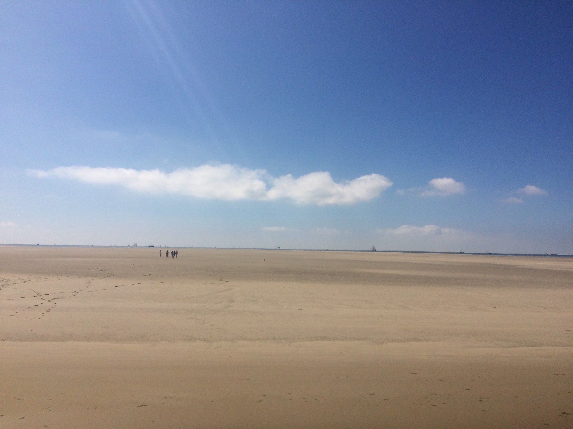 Sandstrand unter strahlend blauem Himmel, in der Ferne spazieren ein paar Menschen.