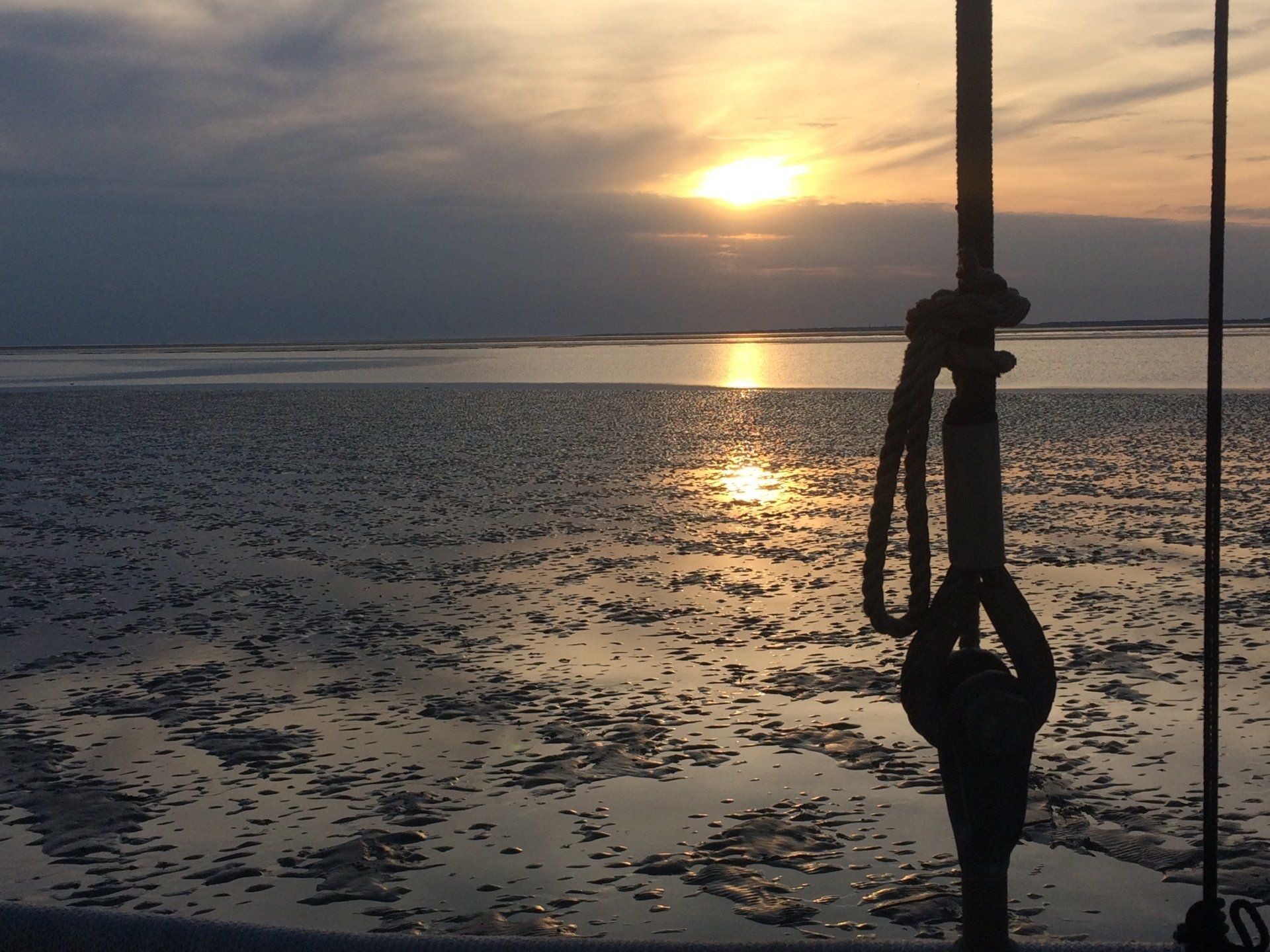 Sonnenuntergang über einer trockengefallen Sandbank auf dem Wattenmeer, Seil im Vordergrund.