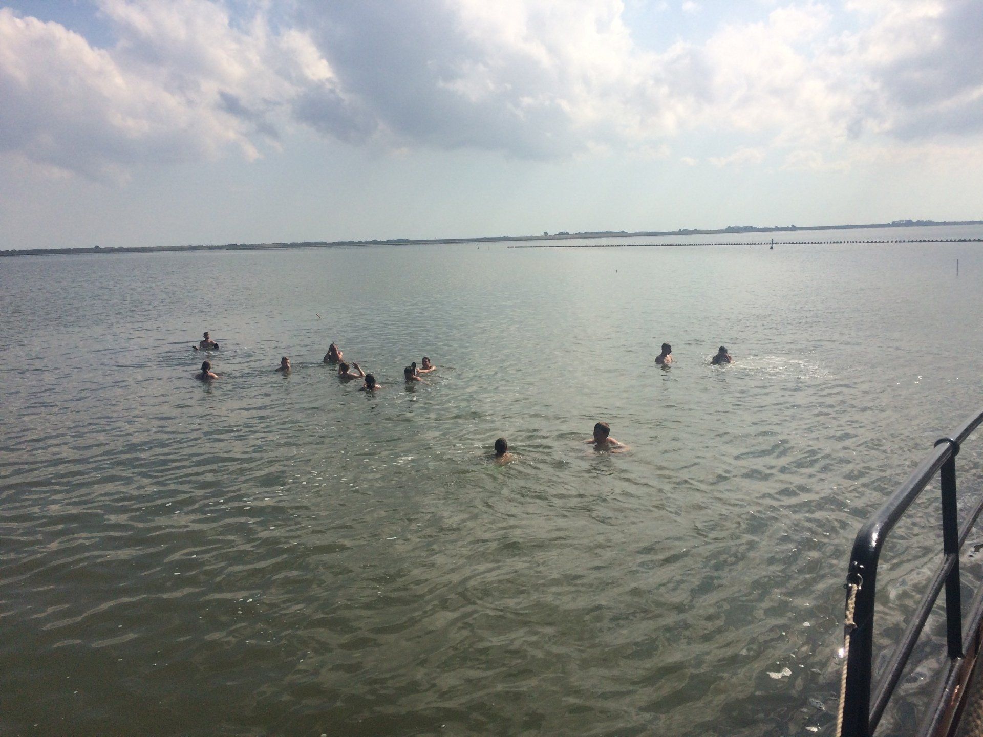 Menschen, die unter einem bewölkten Himmel in einem Gewässer schwimmen; vom Rand eines Bootes aus gesehen.