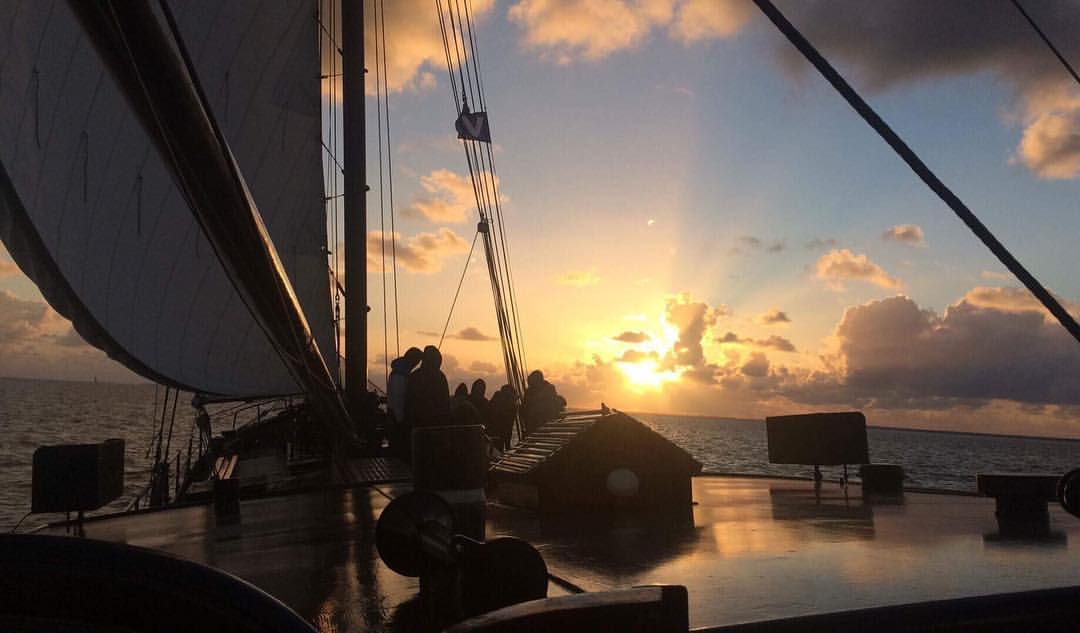 Segelbootdeck bei Sonnenuntergang, Silhouetten von Figuren, goldener Himmel, Ozean.