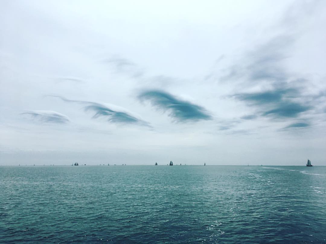 Ozean mit Segelbooten unter einem bewölkten, grauen Himmel.