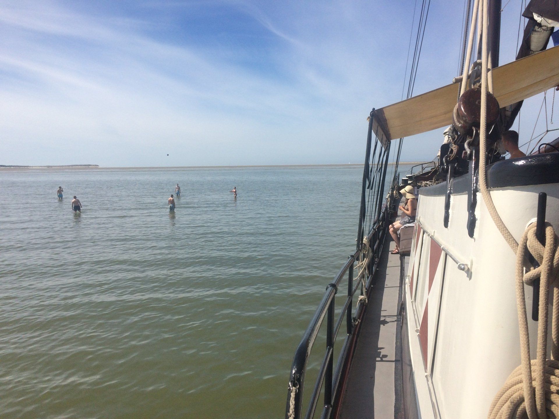 Segelboot auf dem Wasser, Blick auf watende Menschen, blauer Himmel.