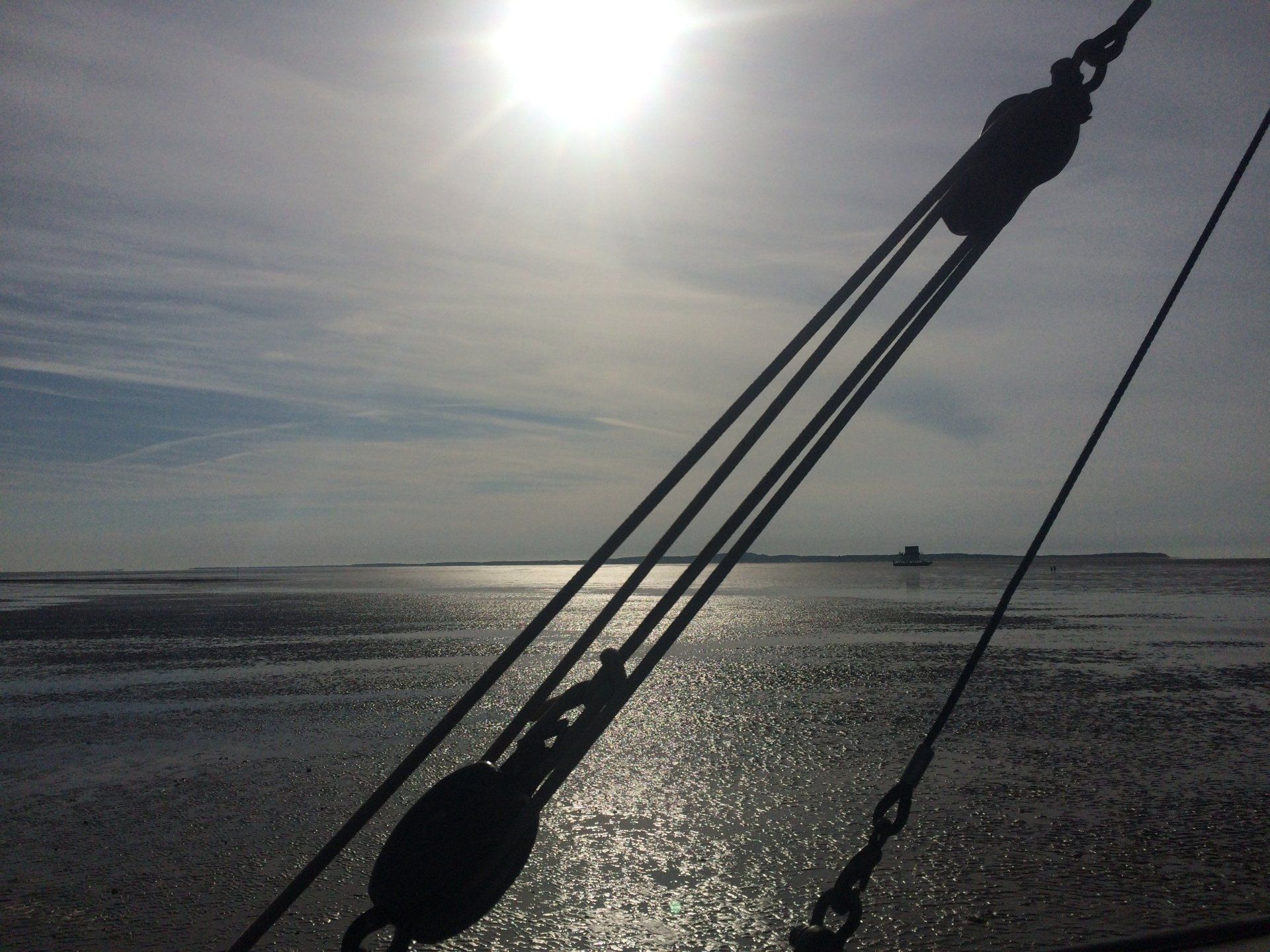 Silhouette einer Schiffstakelage vor einer sonnenbeschienenen Meeresszene bei Ebbe.
