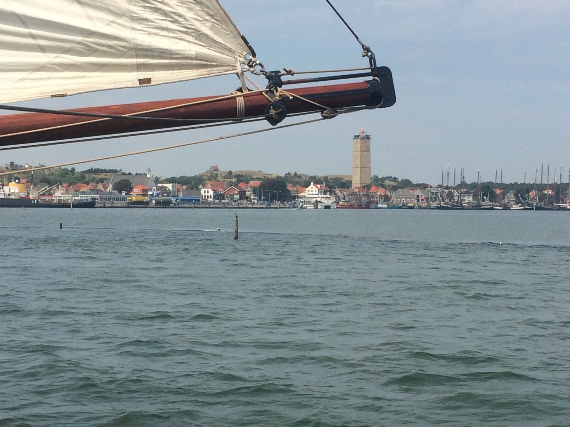 An einem sonnigen Tag segelt ein Segelboot an einer Küstenstadt mit einem hohen Turm vorbei.