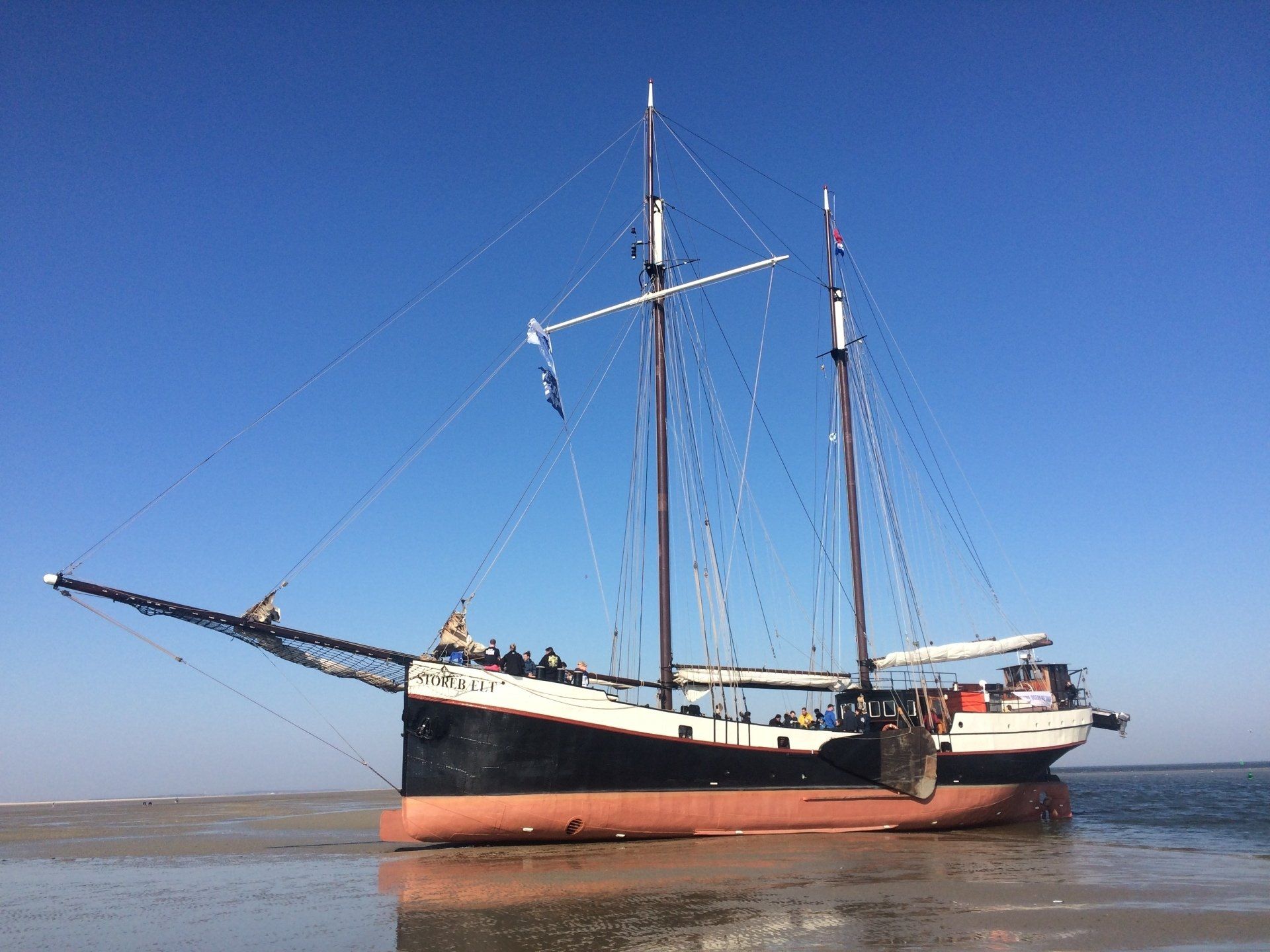 Plattboden trockengefallen auf dem Wattt; schwarzer Rumpf, rote Wasserlinie, blauer Himmel.