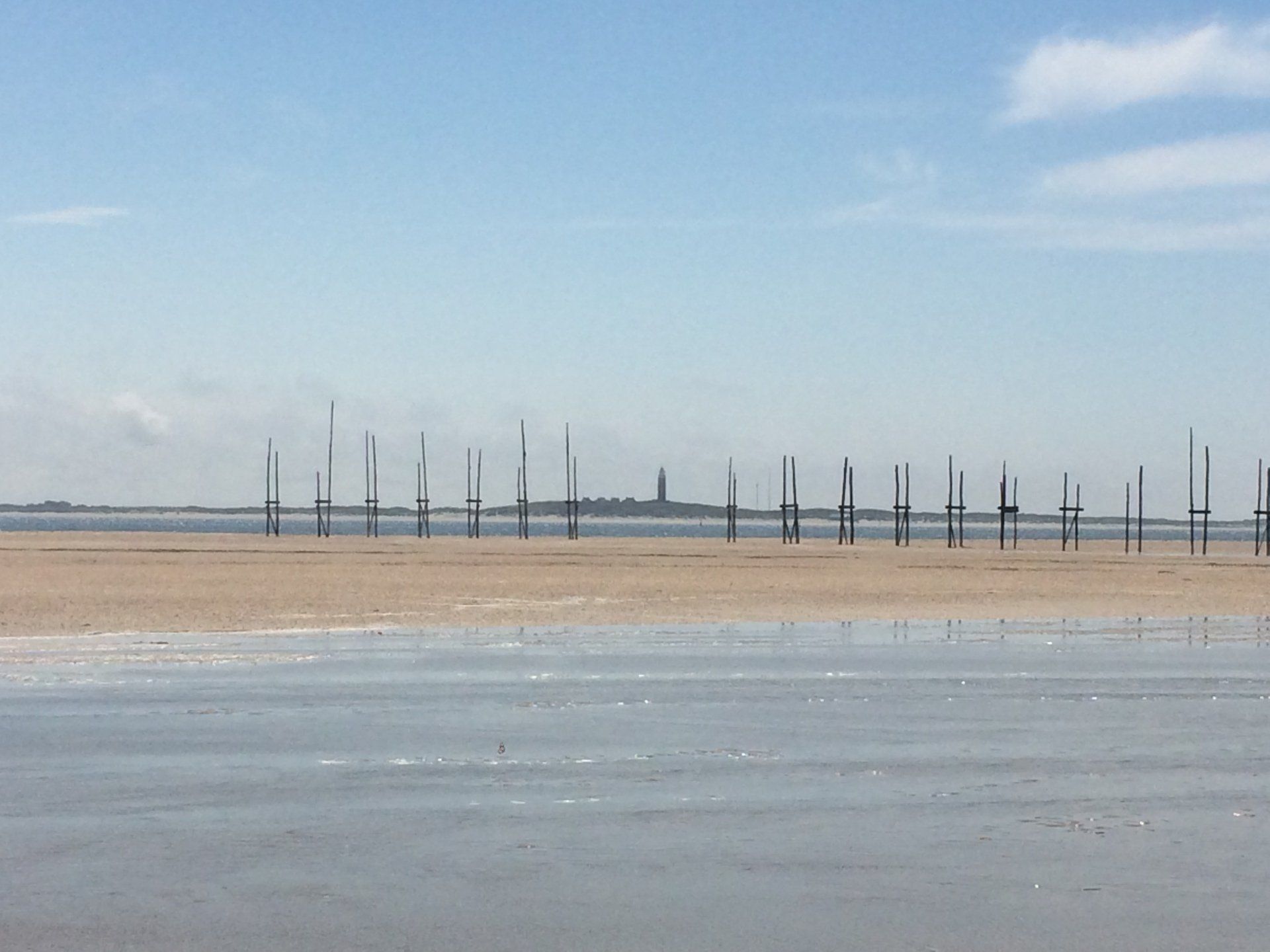 Sandstrand mit Holzpfosten, entfernter Landmasse und hellblauem Himmel.