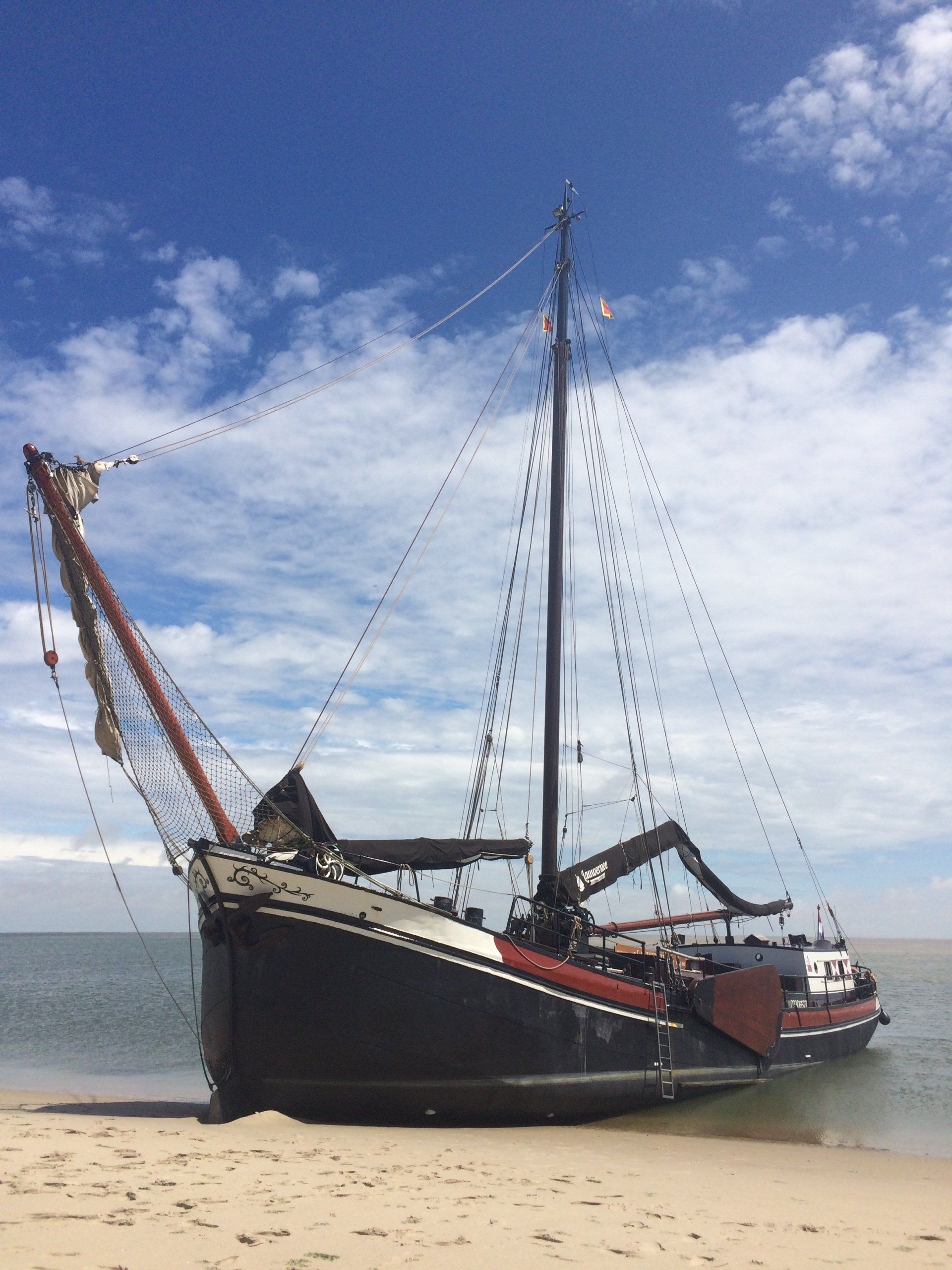 Auf Sand gestrandetes Segelboot vor blauem Himmel mit dünnen Wolken.