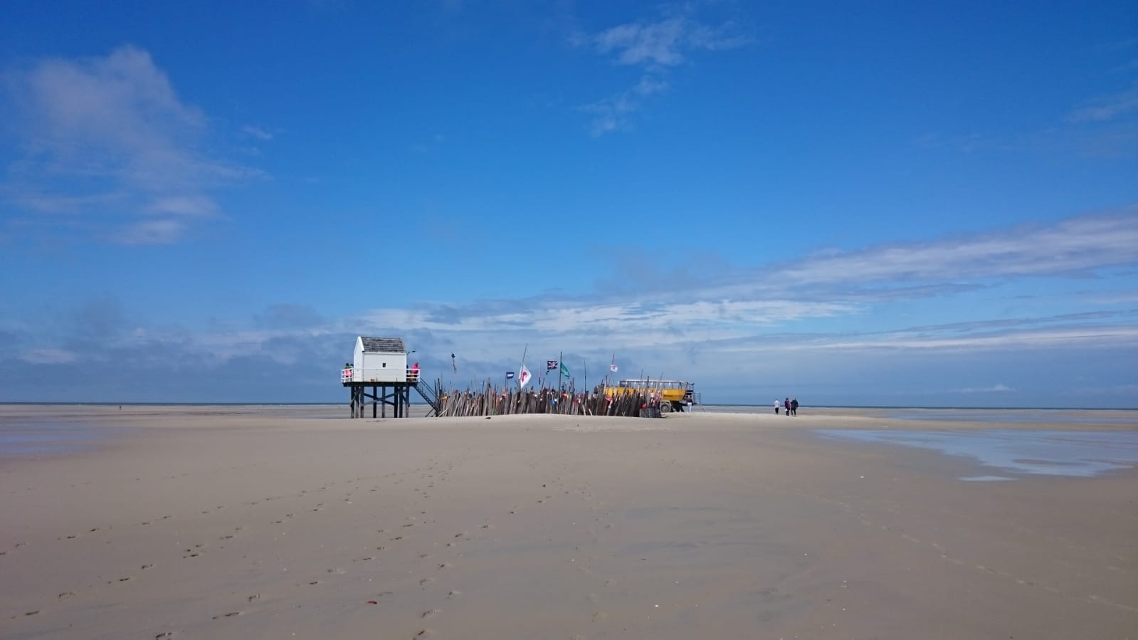 Unter einem strahlend blauen Himmel versammelten sich Menschen in der Nähe eines Gebäudes an einem Sandstrand.