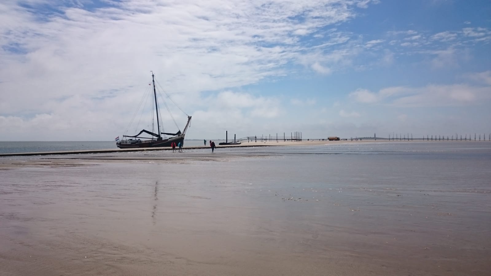 Ein Segelboot liegt auf einer Sandbank nahe der Wasserkante unter einem bewölkten blauen Himmel.