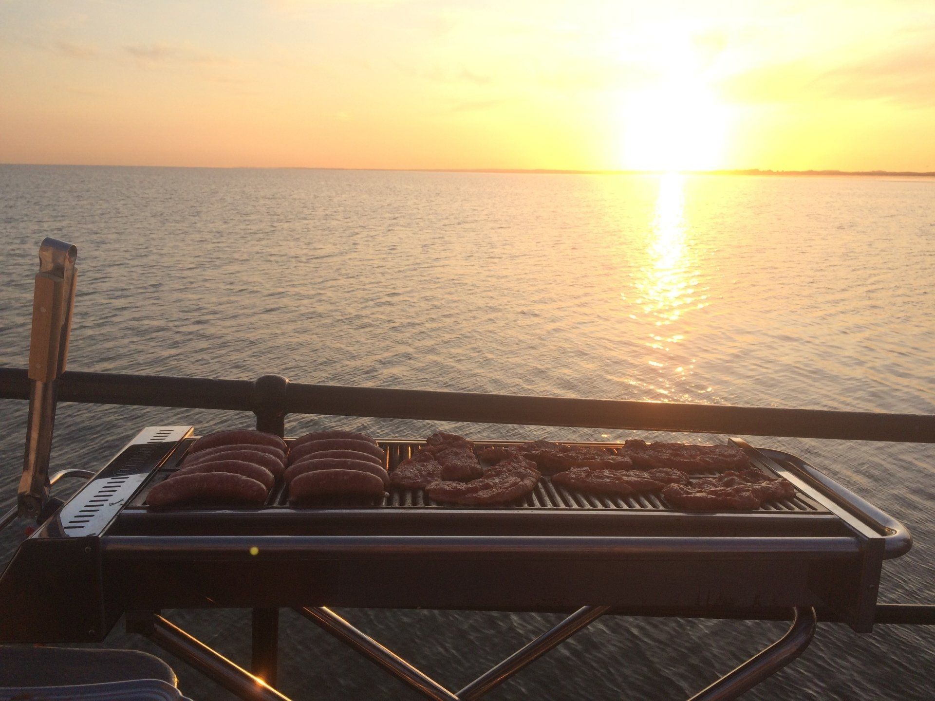 Fleisch grillen auf einem Pier bei Sonnenuntergang über dem Meer.