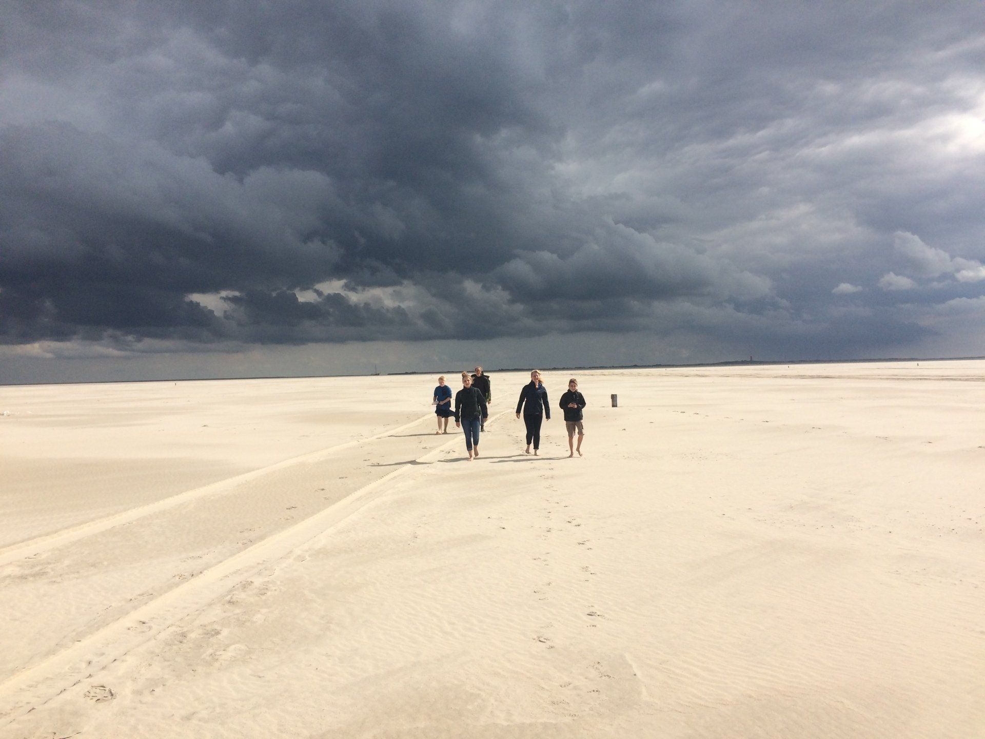Eine Gruppe von Menschen läuft unter einem dunklen, stürmischen Himmel auf einer Sanddüne.