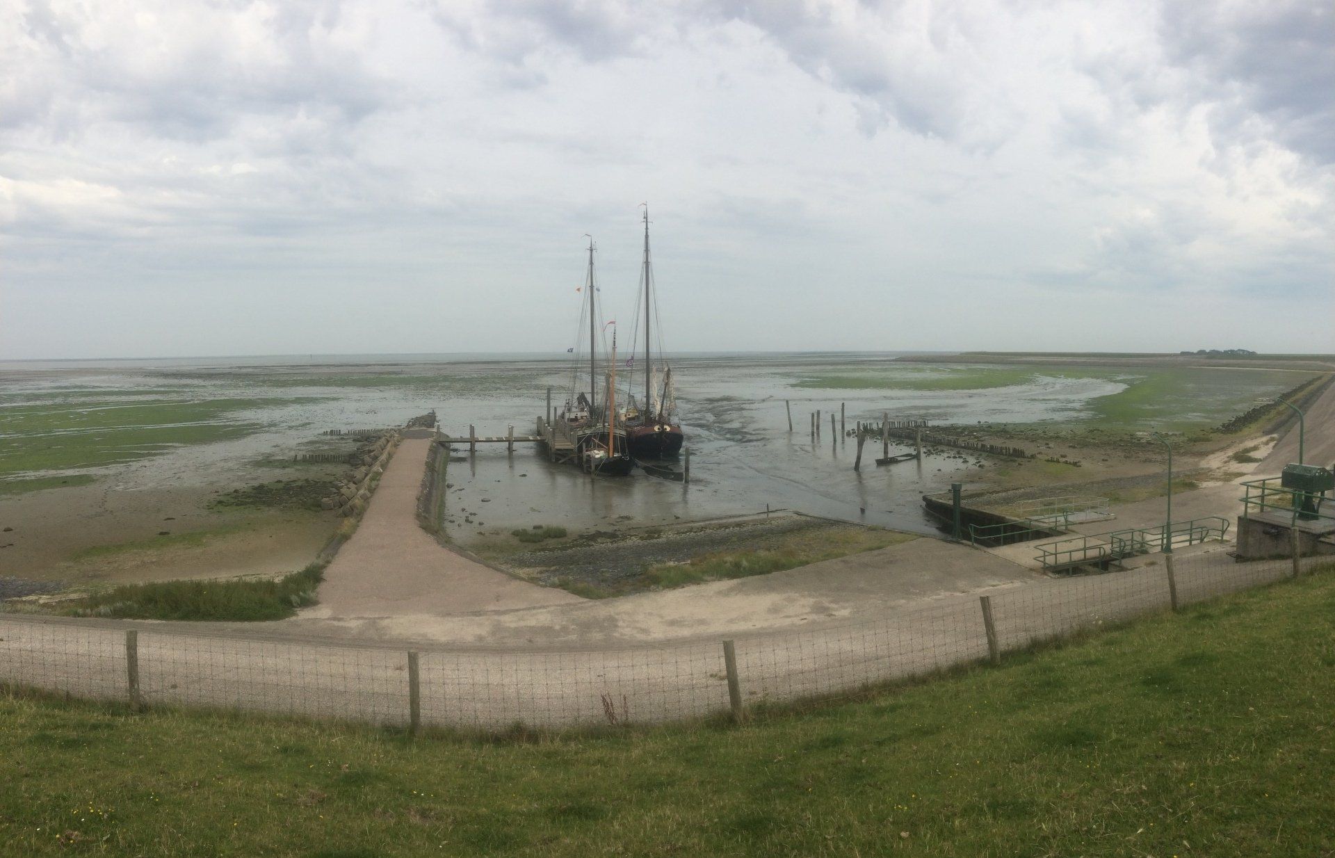 Ein Segelboot liegt in einem Hafen, umgeben von einem riesigen Sumpfgebiet bei Ebbe unter einem bewölkten Himmel.