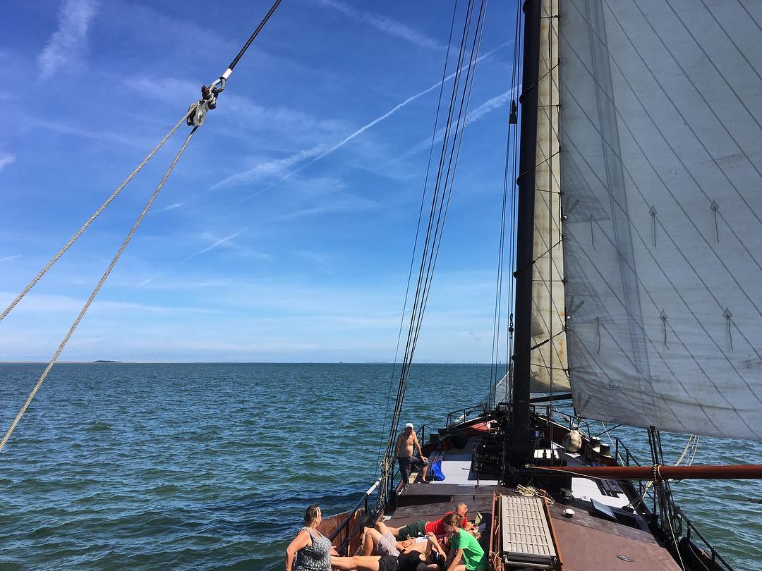 Ein Segelboot segelt unter blauem Himmel auf dem Meer, und die Leute entspannen sich auf dem Deck.